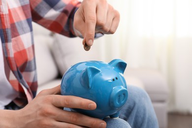 Photo of Man putting coin in piggy bank at home, closeup