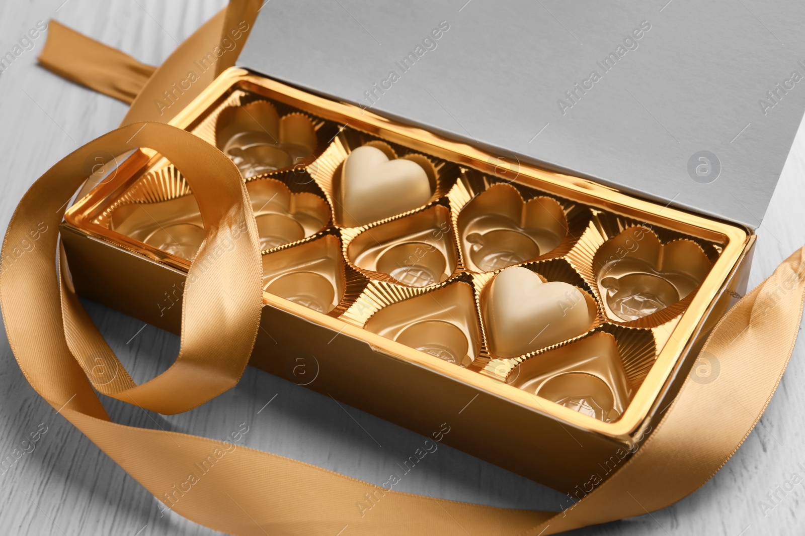 Photo of Partially empty box of chocolate candies on white wooden table