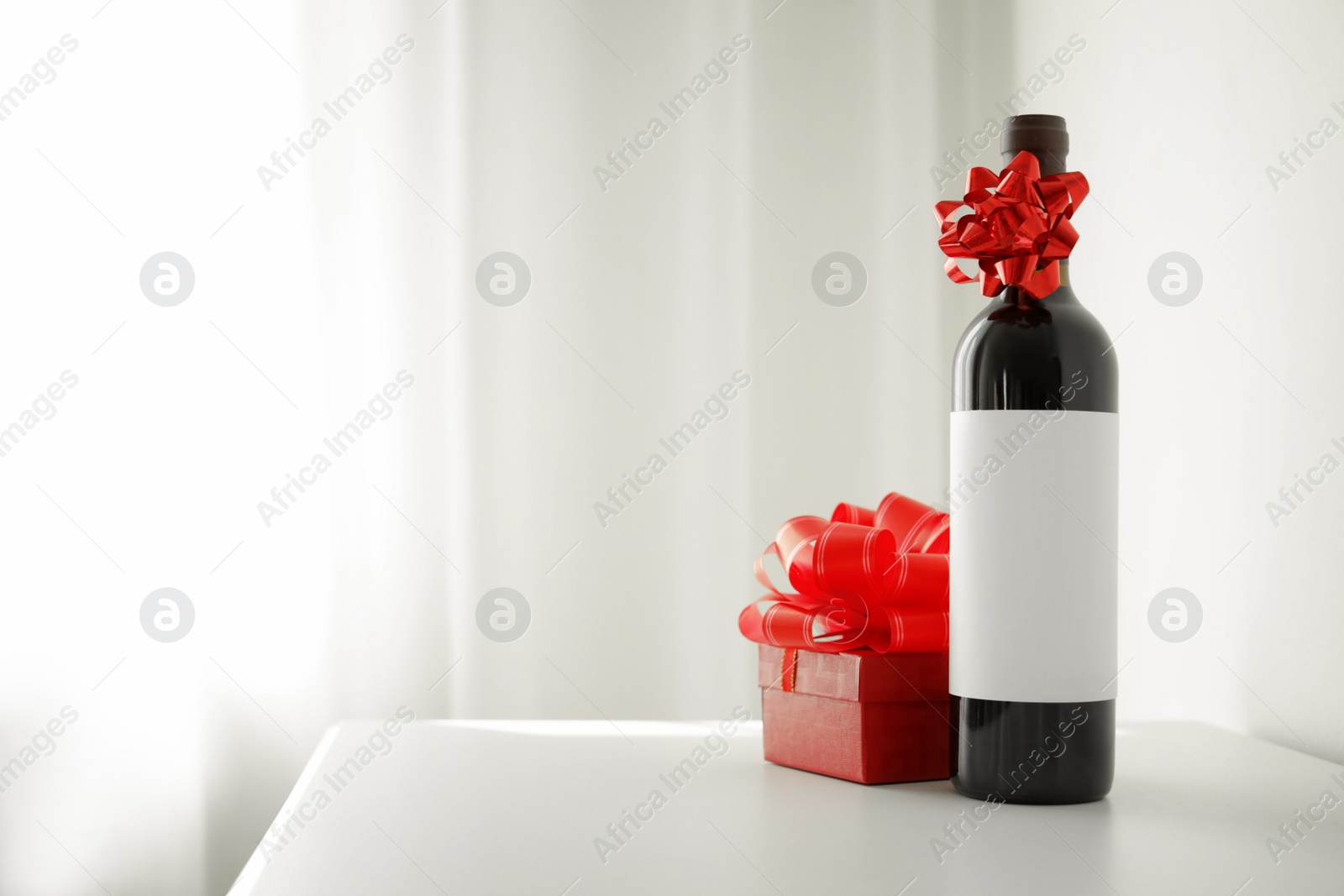 Photo of Bottle of wine and gift box on table in light room. Space for text