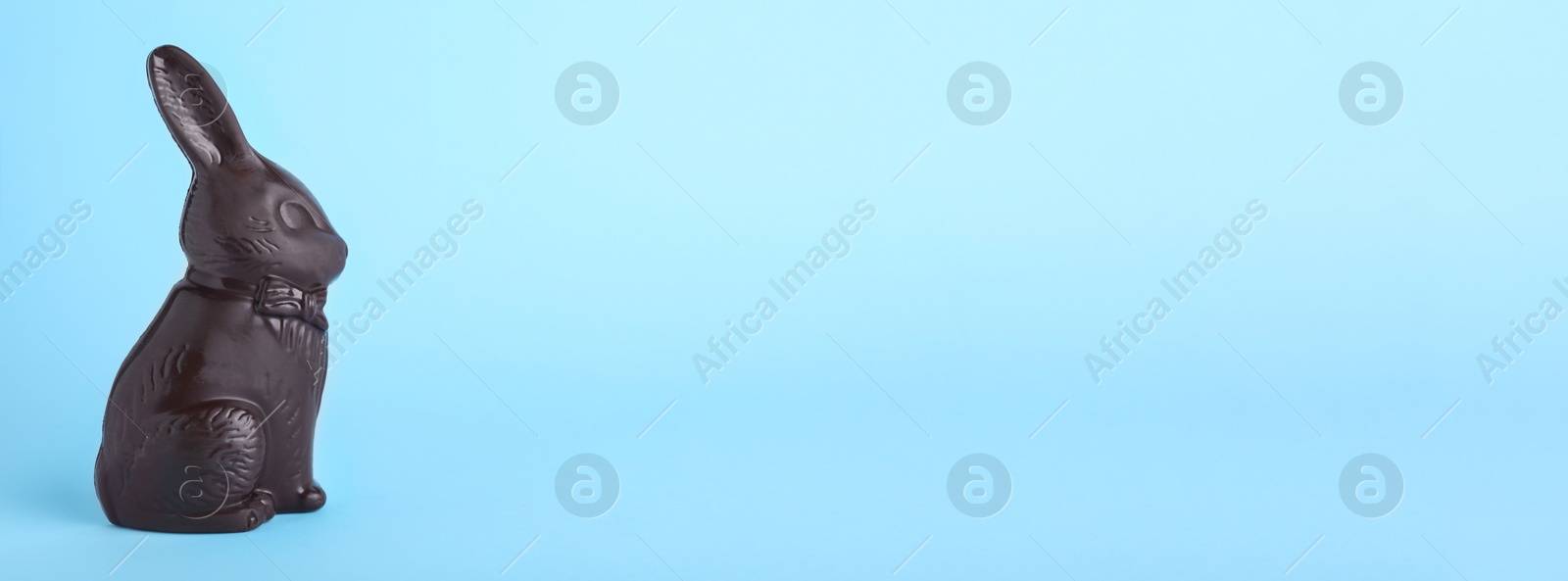 Photo of Dark chocolate Easter bunny on light blue background, space for text