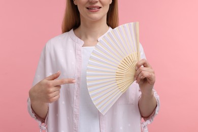 Photo of Woman with hand fan pointing on pink background, closeup