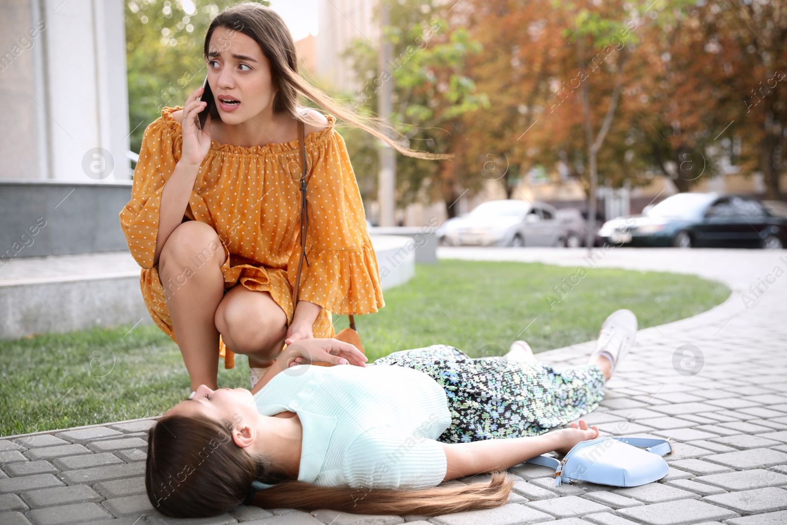 Photo of Woman calling ambulance to help unconscious person with heart attack on city street