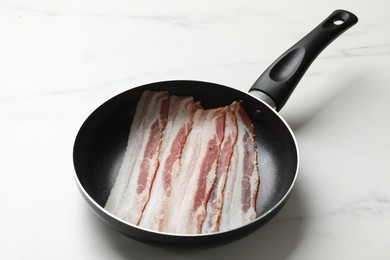 Photo of Slices of raw bacon in frying pan on white marble table, closeup