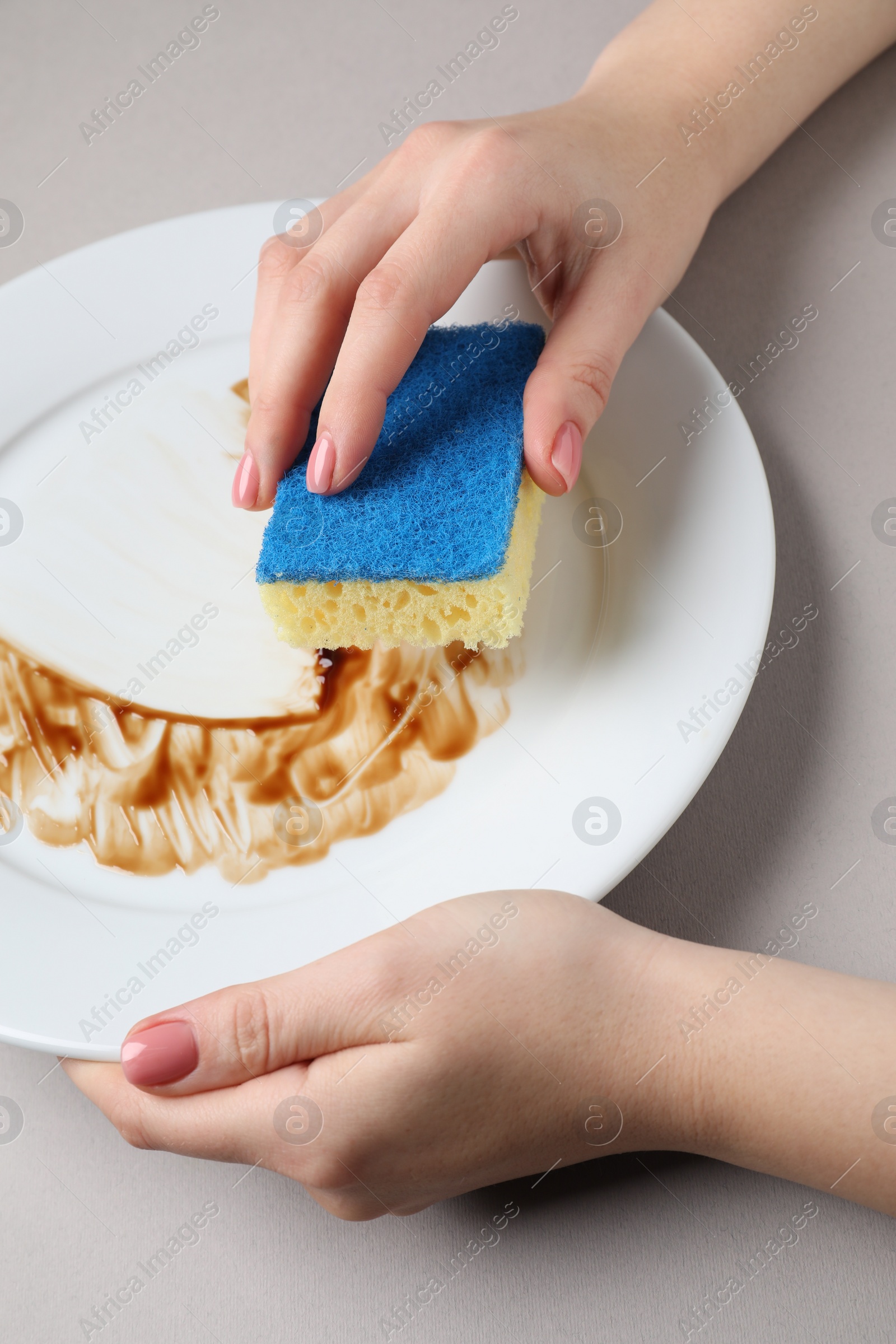 Photo of Woman washing dirty plate with sponge on light grey background, closeup