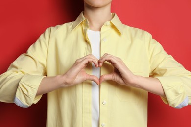 Woman making heart with hands on red background, closeup