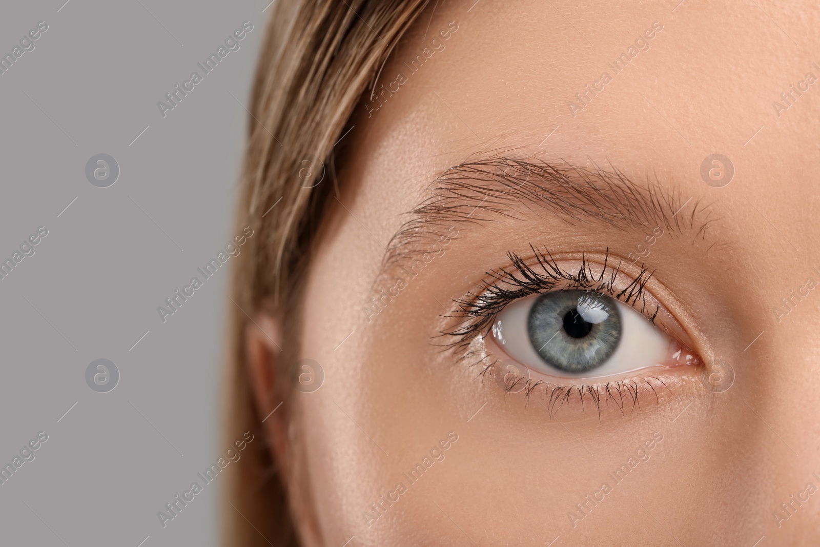 Photo of Woman with long eyelashes after mascara applying against grey background, closeup