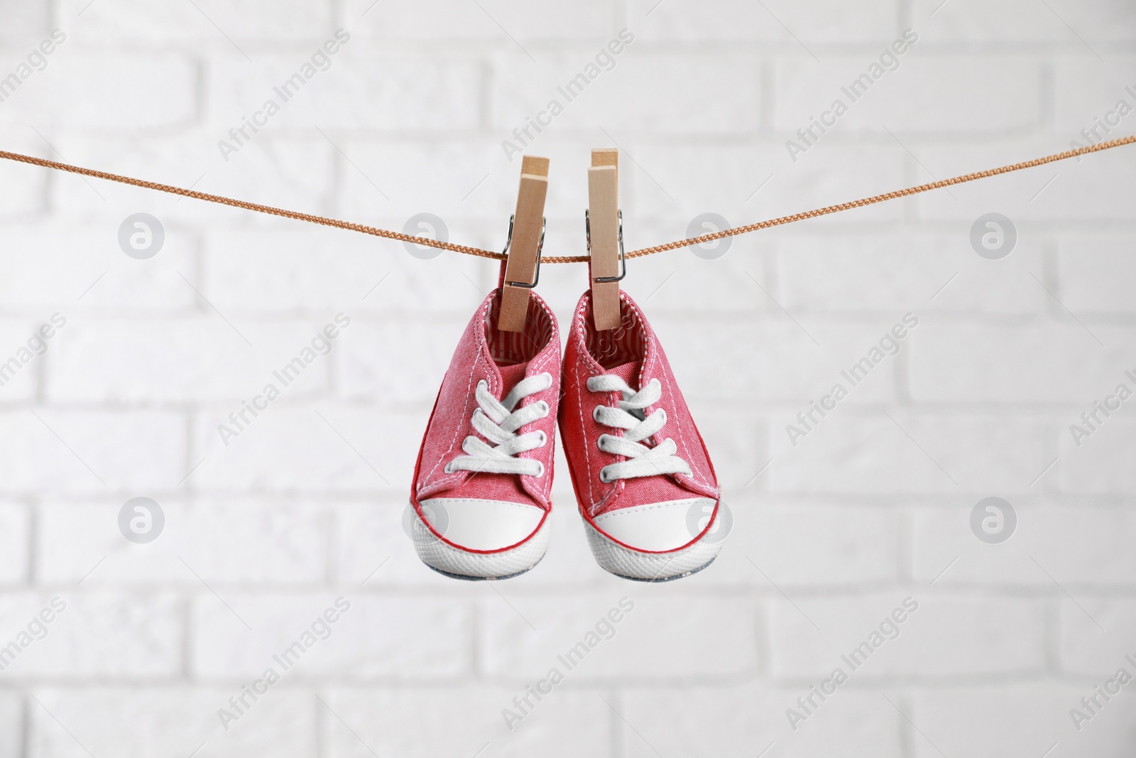 Photo of Cute pink baby sneakers drying on washing line against white brick wall