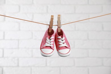 Photo of Cute pink baby sneakers drying on washing line against white brick wall