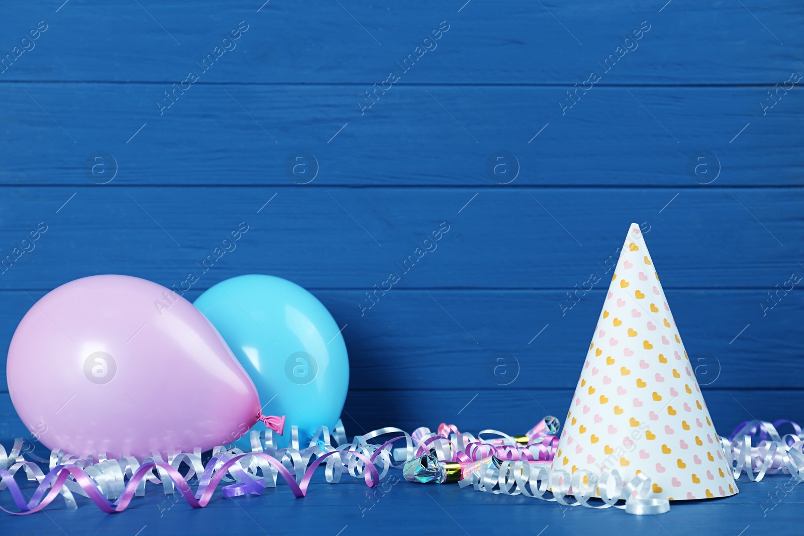 Photo of Colorful serpentine streamers and other party accessories on blue wooden table. Space for text