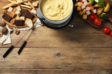 Tasty melted cheese in fondue pot, forks and snacks on wooden table, flat lay. Space for text