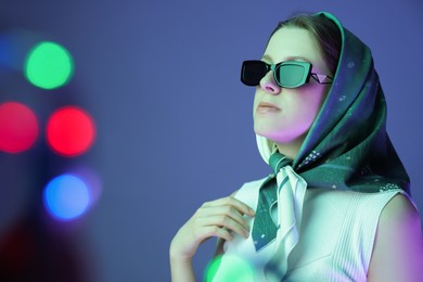 Portrait of beautiful young woman with sunglasses on color background with neon lights. Bokeh effect