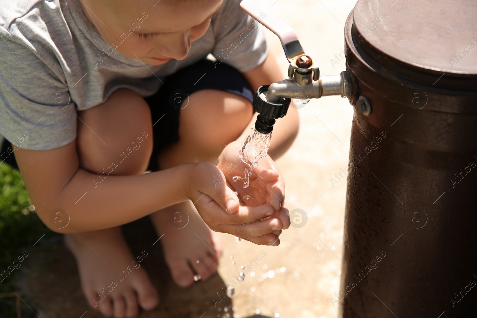 Photo of Water scarcity. Little boy drinking water from tap outdoors, closeup