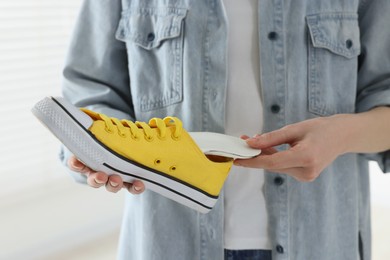 Woman putting orthopedic insole into shoe on blurred background, closeup. Foot care
