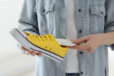 Photo of Woman putting orthopedic insole into shoe on blurred background, closeup. Foot care