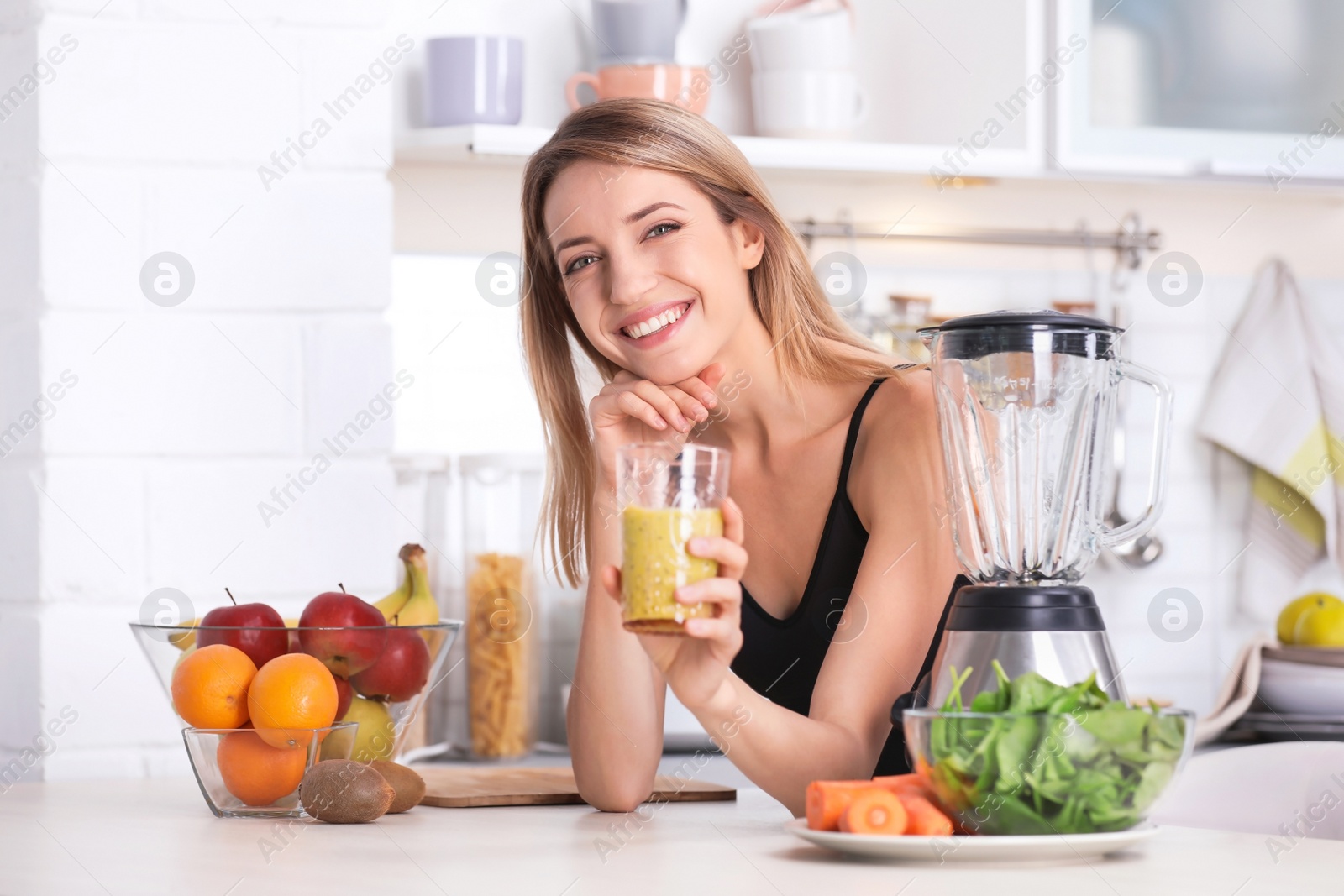 Photo of Young woman with glass of tasty healthy smoothie at table in kitchen