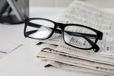 Stack of newspapers and glasses on white table, closeup