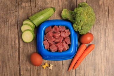 Photo of Raw meat in bowl, products and vitamins for pet on wooden background, flat lay