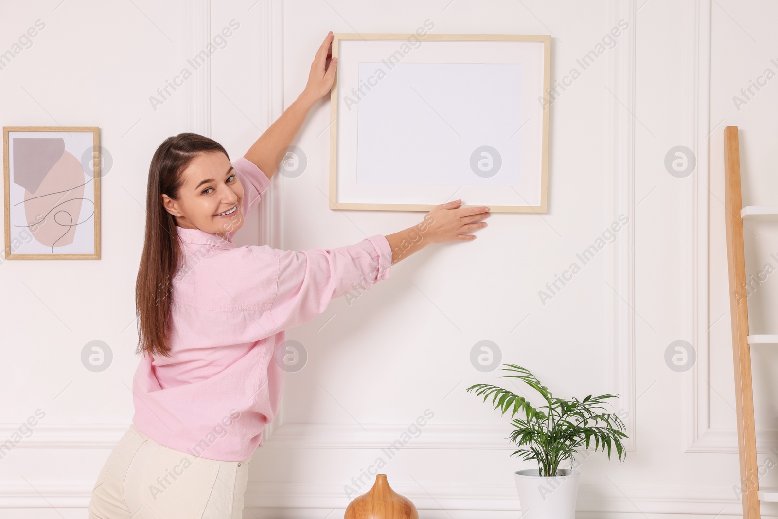 Photo of Woman hanging picture frame on white wall at home