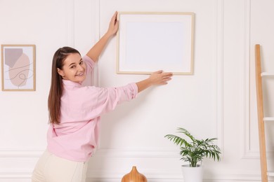 Photo of Woman hanging picture frame on white wall at home