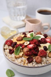 Photo of Oatmeal with freeze dried fruits, nuts and mint on white table