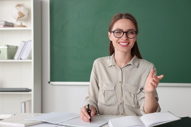 Beautiful young teacher giving lesson at table in classroom