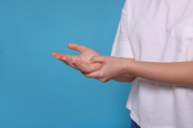 Photo of Senior man suffering from pain in hands on light blue background, closeup. Arthritis symptoms