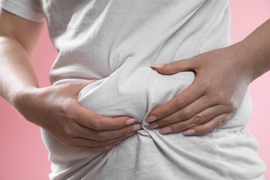 Woman touching belly fat on pink background, closeup. Overweight problem