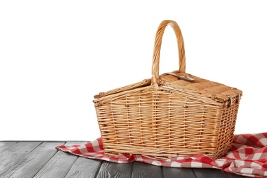 Photo of Closed wicker picnic basket with checkered tablecloth on wooden table against white background