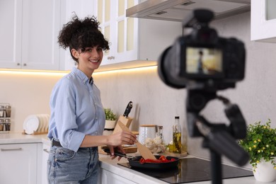 Photo of Smiling food blogger cooking while recording video in kitchen