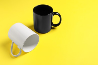 Photo of Black and white ceramic mugs on yellow background. Space for text