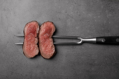 Fork with slices of meat on grey table, top view