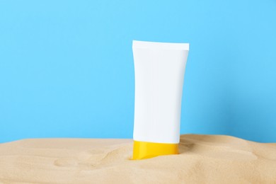 Photo of Suntan product in sand against light blue background. Space for text