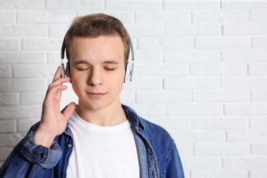 Teen boy listening to music with headphones near brick wall, space for text