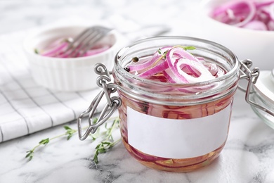 Jar of pickled onions with blank label on marble table