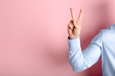 Photo of Young man showing victory gesture on color background. Space for text