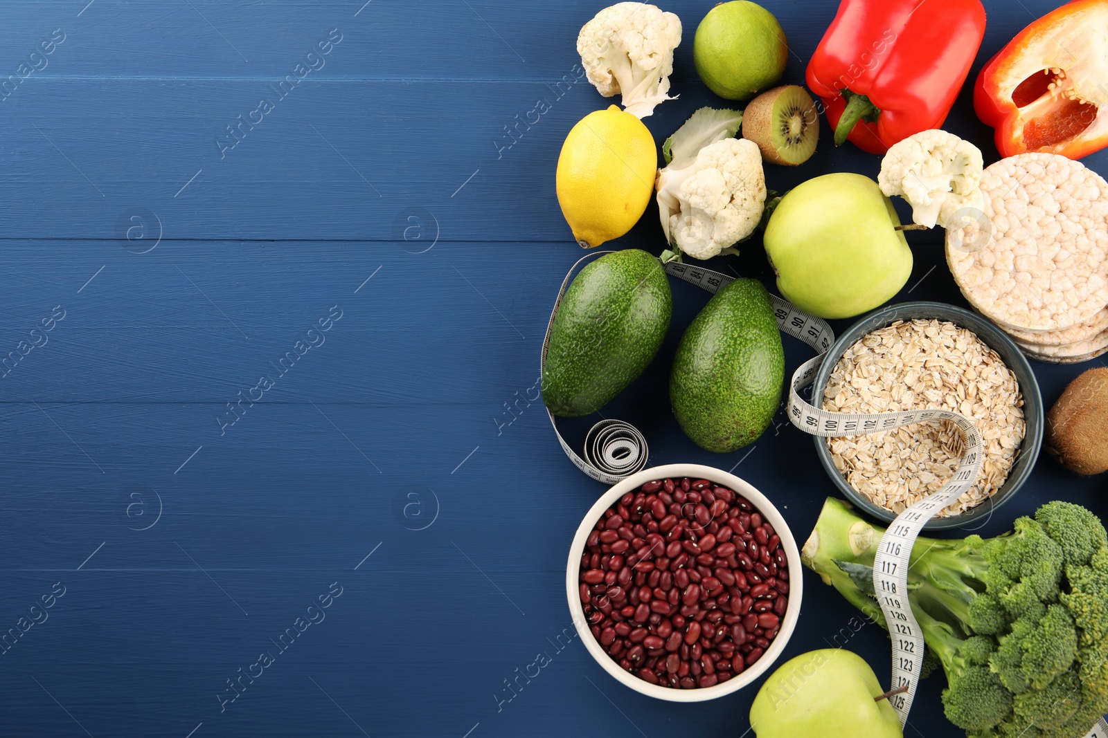 Photo of Healthy diet. Different products and measuring tape on blue wooden table, flat lay with space for text