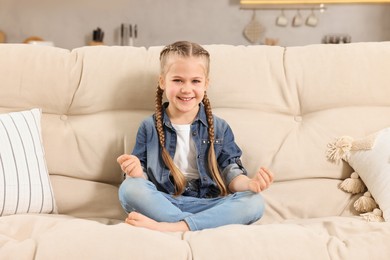 Photo of Little girl meditating on soft sofa at home