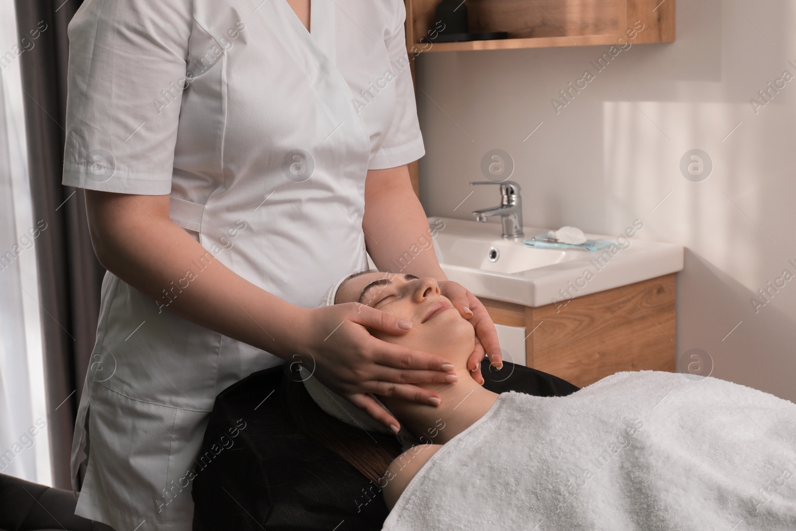 Photo of Cosmetologist making face massage to client in clinic, closeup