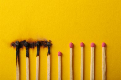 Photo of Burnt and whole matches on yellow background, flat lay. Stop destruction by breaking chain reaction concept