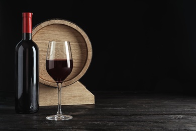 Photo of Glass, bottle and barrel with delicious red wine on table against dark background