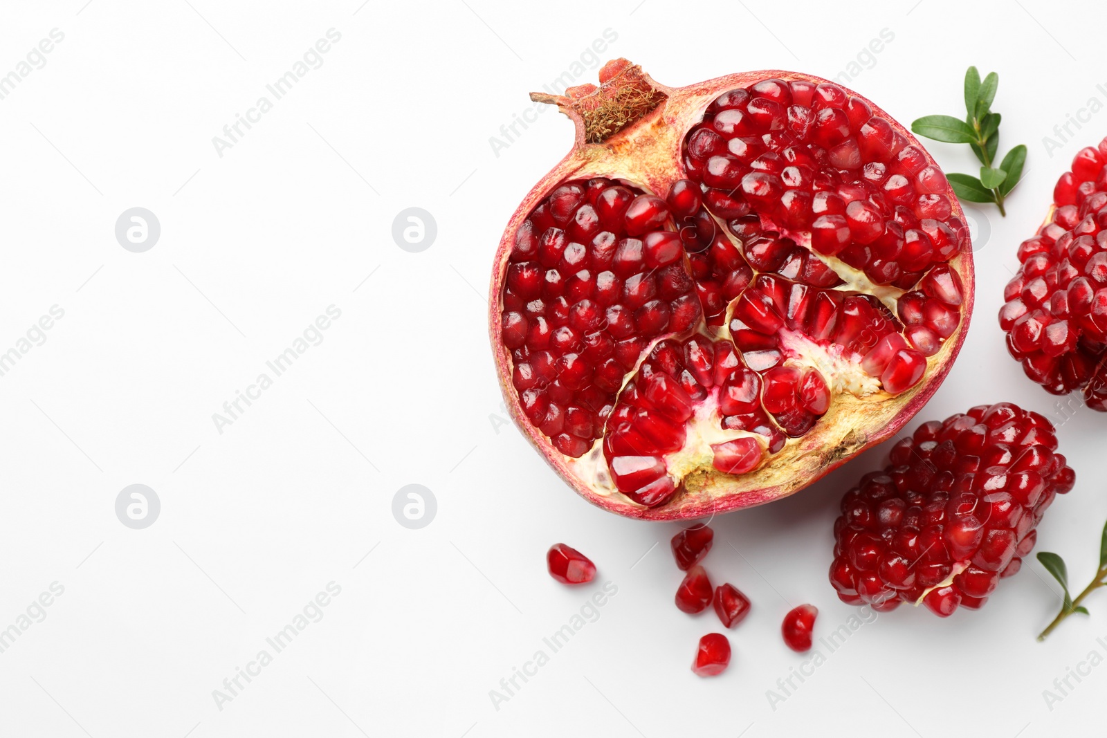 Photo of Cut fresh pomegranate and green leaves on white background, flat lay. Space for text