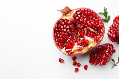 Photo of Cut fresh pomegranate and green leaves on white background, flat lay. Space for text