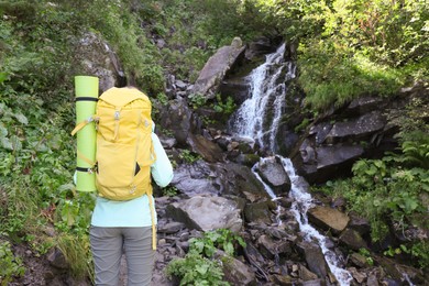 Tourist with backpack near stream in mountains, back view. Space for text