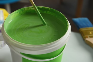 Photo of Plastic bucket of green paint on white table, closeup