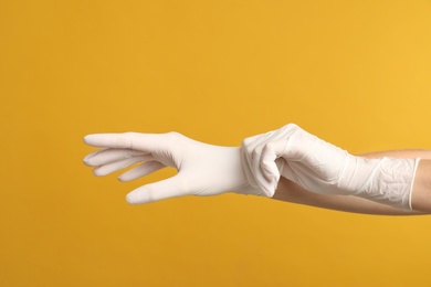 Doctor wearing medical gloves on yellow background, closeup