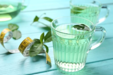 Photo of Herbal diet tea and measuring tape on light blue wooden table, closeup