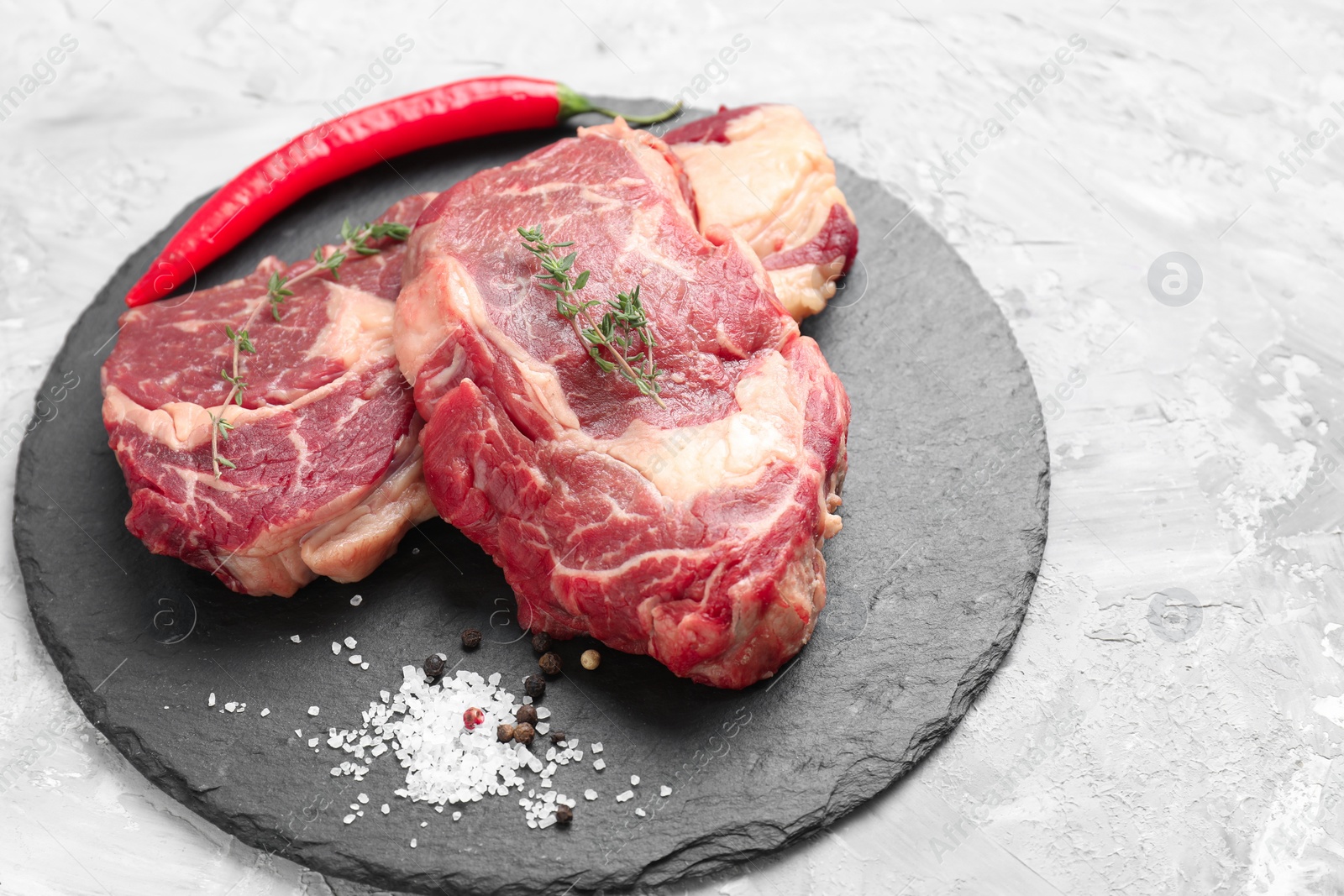 Photo of Fresh raw beef cut with different spices on light grey textured table. Space for text