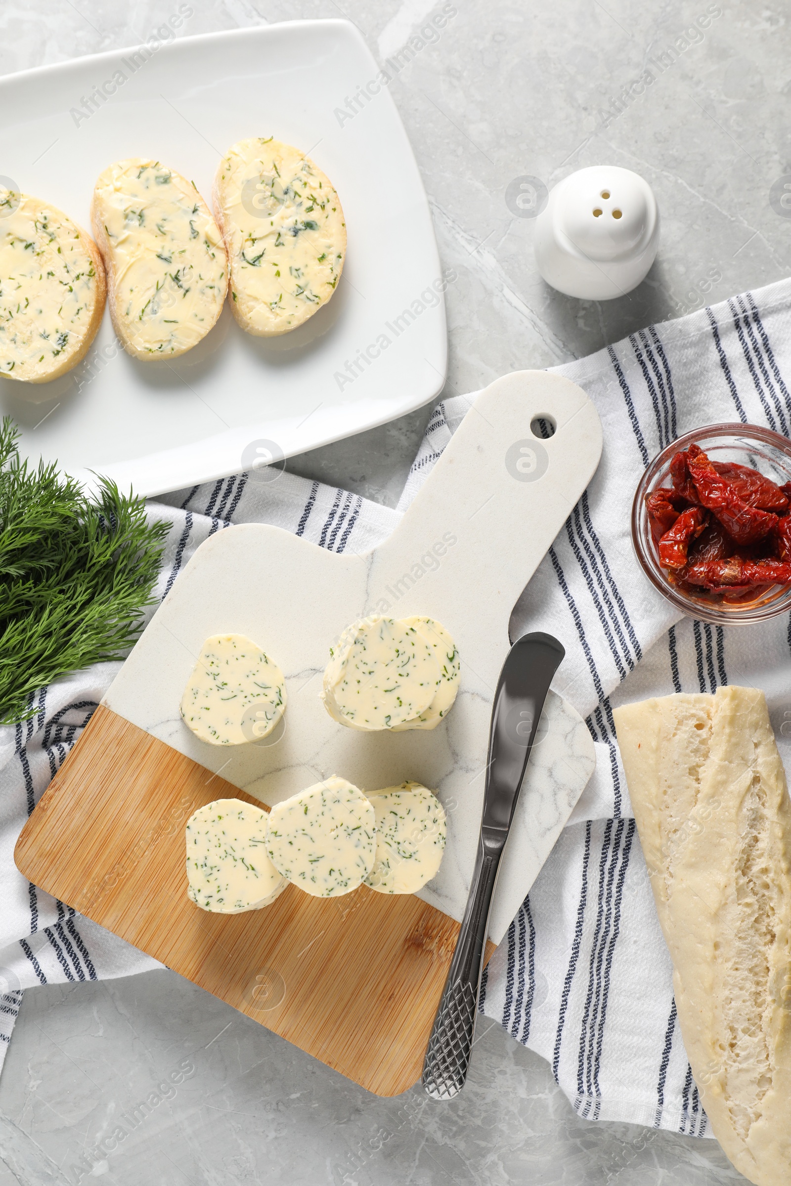 Photo of Tasty butter with dill, chili peppers, bread and knife on grey marble table, top view