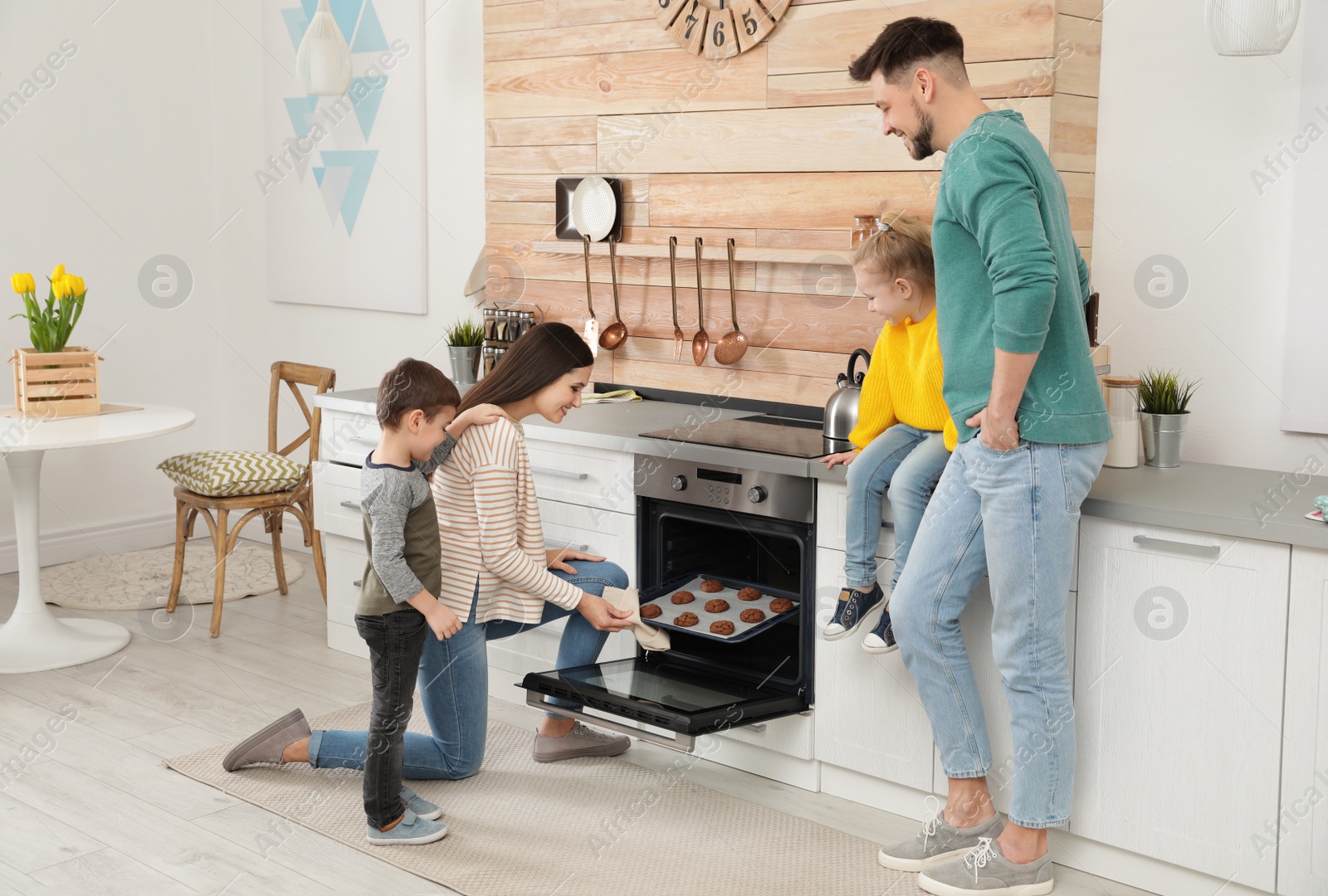 Photo of Woman and her family taking out tray with baked cookies from oven in kitchen