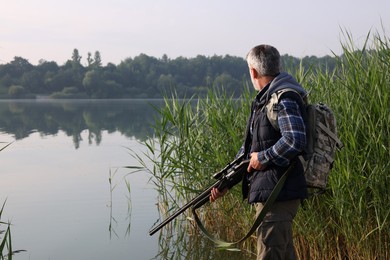 Photo of Man with hunting rifle near lake outdoors. Space for text